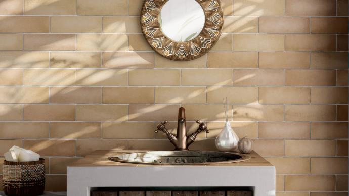 Bathroom vanity with Perfection gold matte ceramic tile on the wall, a round mirror, and a copper faucet.