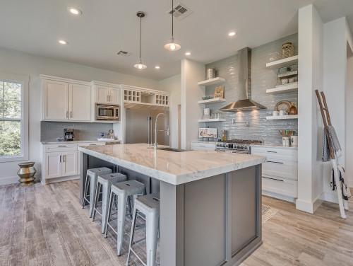 Modern kitchen with a large island and a grey subway tile backsplash behind the stove and open shelving.