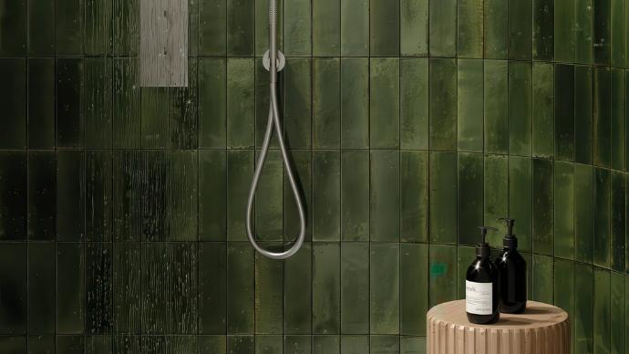 A close-up of a shower wall featuring a glossy, Dark Green Subway Tile laid vertically