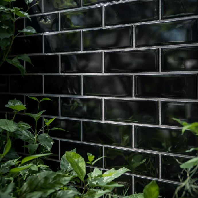 Close-up of glossy black subway tiles with light-colored grout, surrounded by lush green foliage.