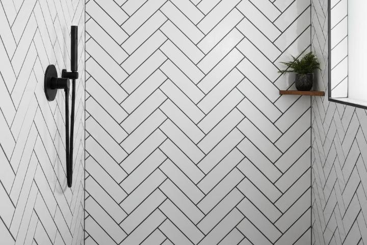 White subway tiles installed in herringbone pattern on modern bathroom shower wall with dark grout lines