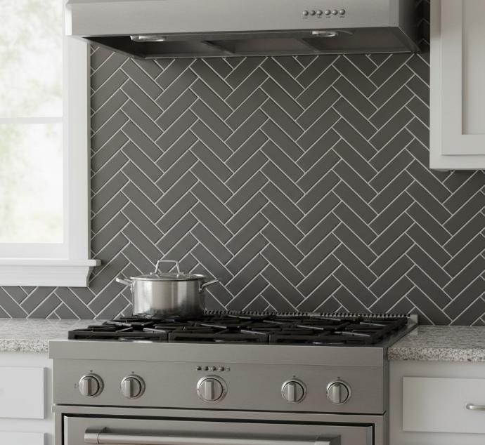 A striking dark grey herringbone tile backsplash provides a bold backdrop to a professional-style stainless steel gas range and hood.