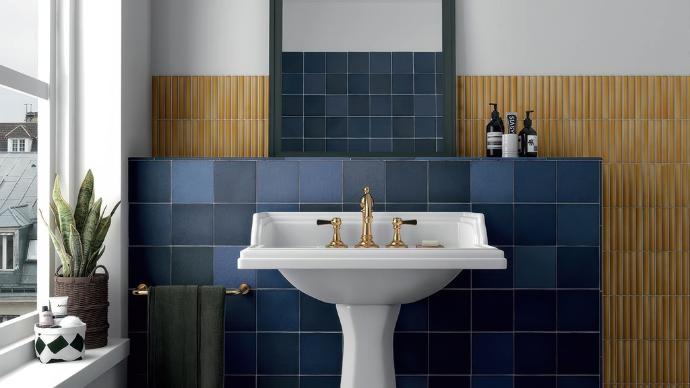 A richly colored bathroom featuring a pedestal sink with brass fixtures set against a wall tiled with 5x5 perfection subway tile.