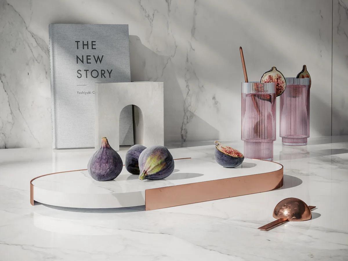 Statuario Principe porcelain slabs surface styled with figs, pink glasses, and a book
