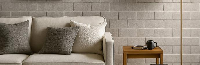 A contemporary living room featuring a neutral-toned sofa against a focal accent wall of fabric-look ceramic subway tiles