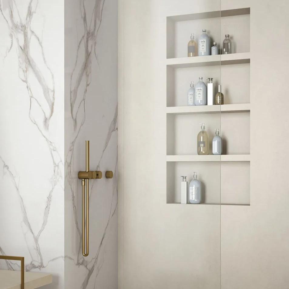 Calacatta Oro porcelain slabs featuring built in shelving niche with gold shower fixtures in bathroom.
