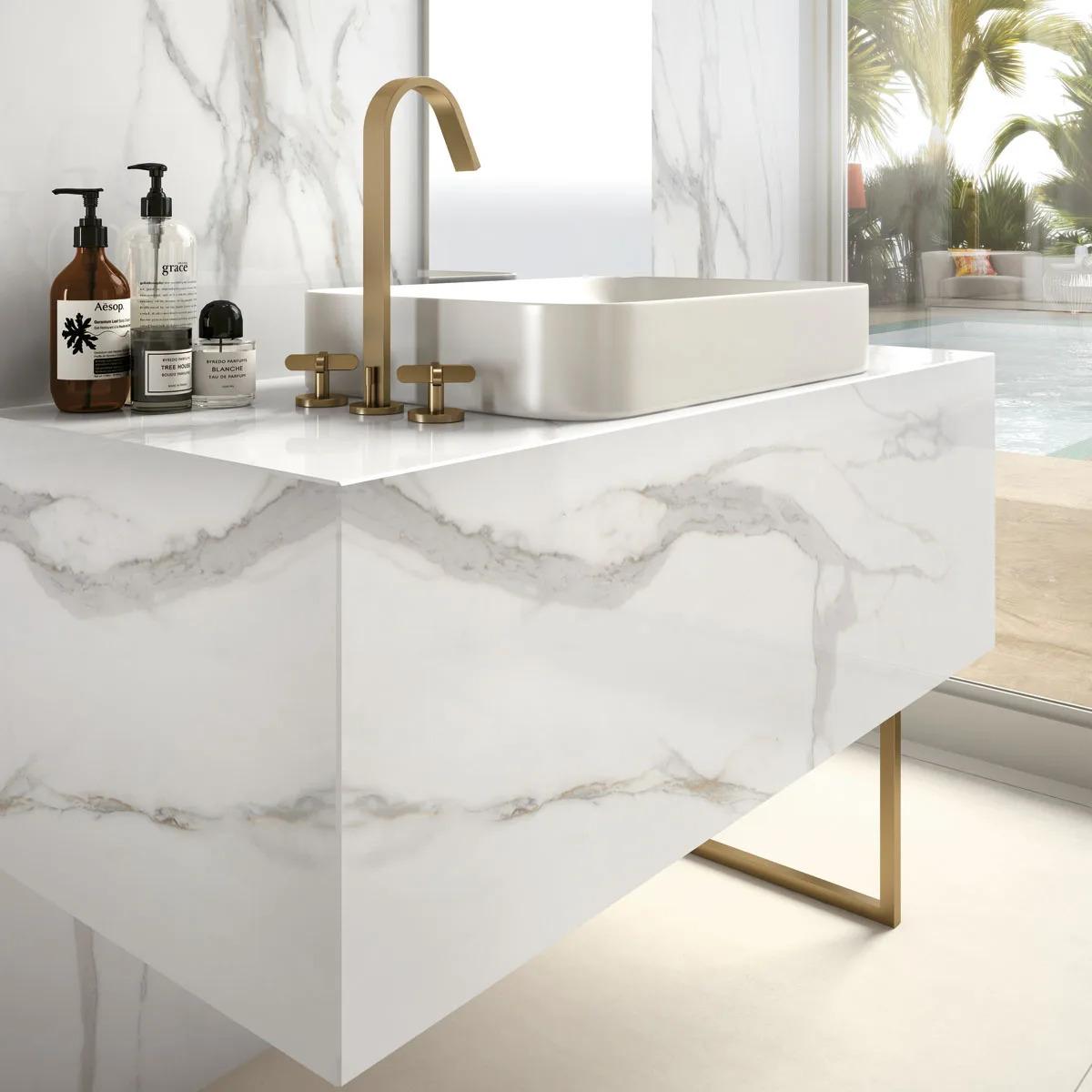 Calacatta Oro porcelain slabs on waterfall edge vanity with gold hardware and tropical view background.