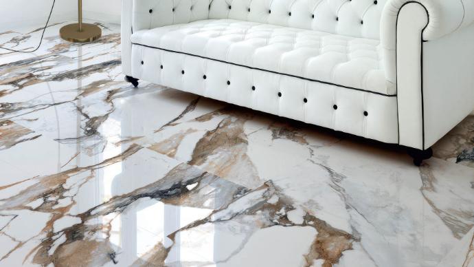 High-gloss marble-look porcelain floor tiles with bold veining and a white tufted sofa in a modern interior.