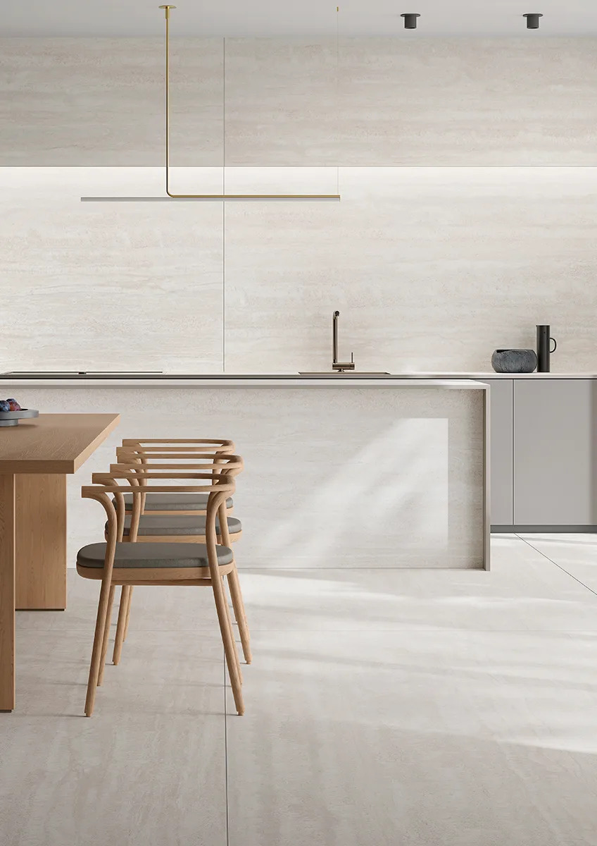Travertino Bianco porcelain slabs throughout open kitchen with wooden chairs and seamless light design.