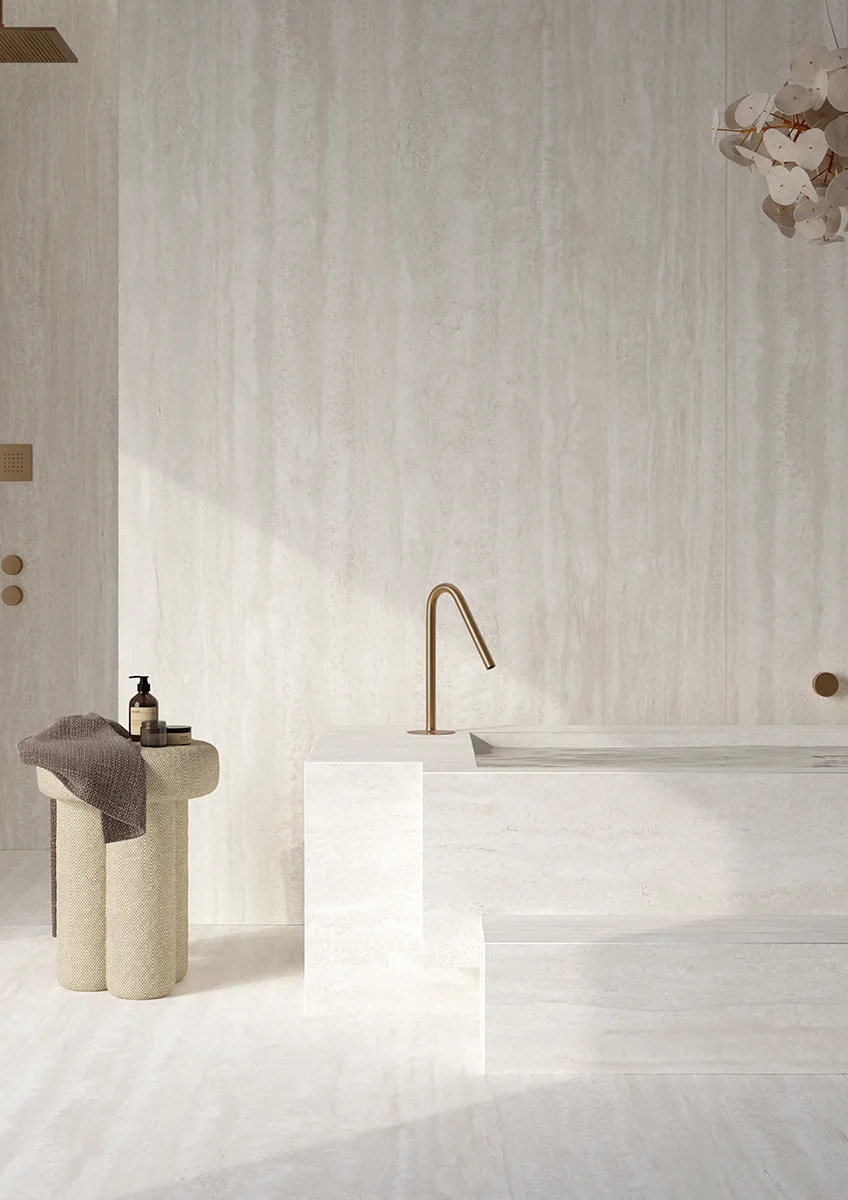 Travertino Bianco porcelain slabs in serene bathroom setting with freestanding vanity and gold faucet detail.