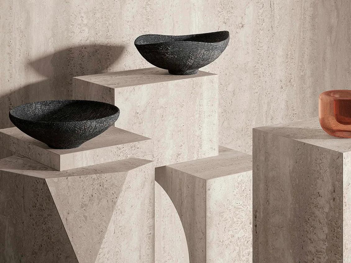 Display pedestals made from Travertino Chiaro porcelain slabs showcasing decorative black bowls and orange vase.