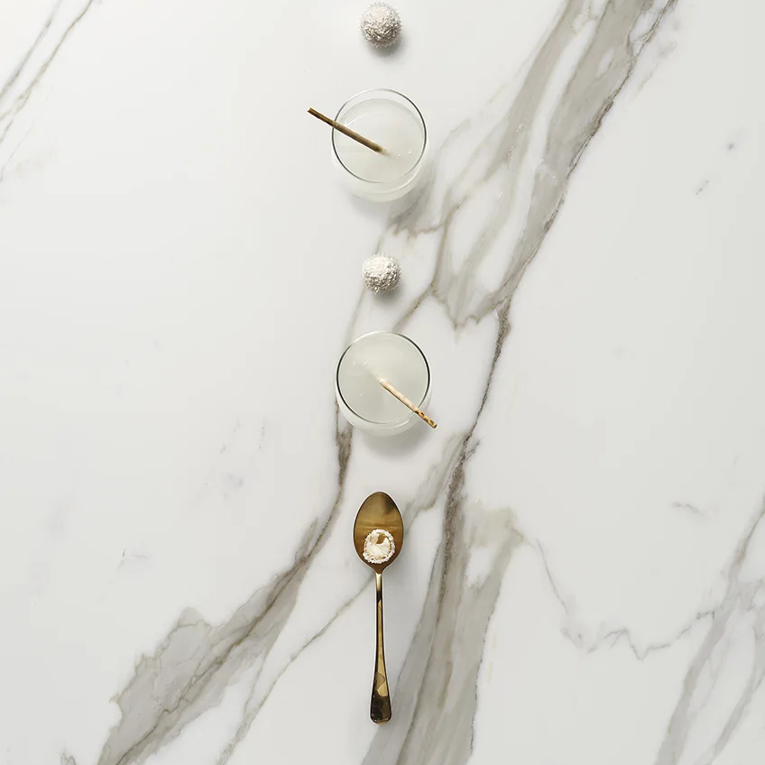 Défense porcelain slabs white marble surface featuring cocktail glasses and gold serving spoon.