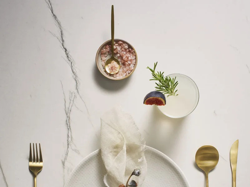 Elegant table setting on Calacatta Brasile porcelain slabs with gold cutlery and cocktails.
