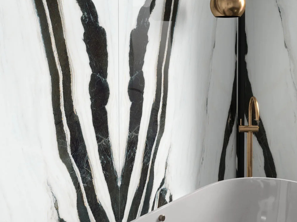 Panda White porcelain slabs bathroom wall behind freestanding tub with brass rain shower.
