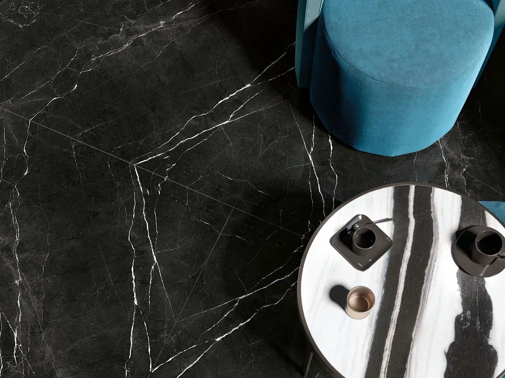 Top down view of Nero Marquinia porcelain slabs flooring with teal chair and marble table.