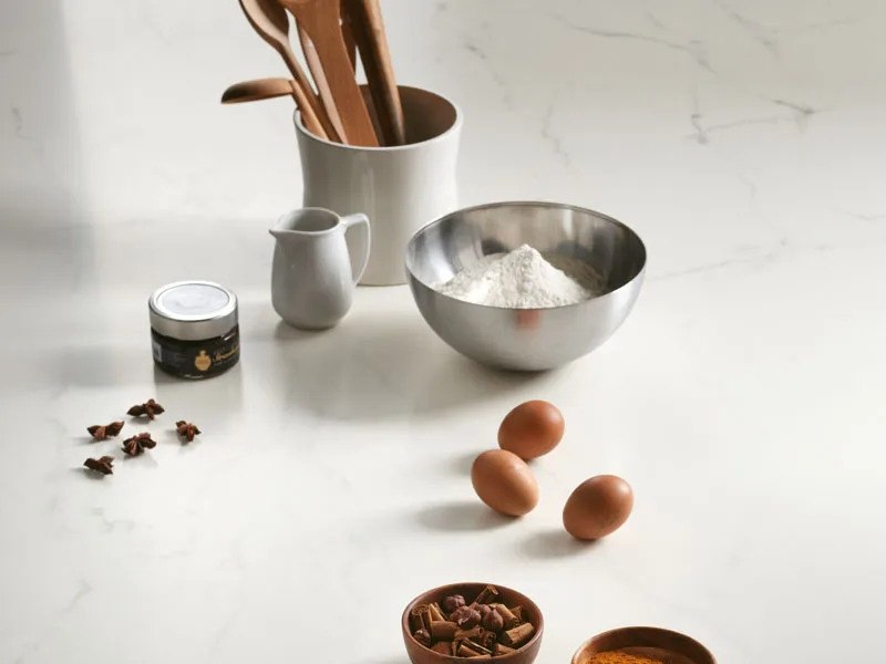 Kitchen countertop made from Calacatta Glory porcelain slabs with baking ingredients and wooden utensils.