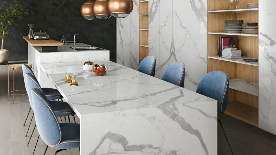 Kitchen island featuring Classic Statuario porcelain slabs with waterfall edge and blue bar stools.