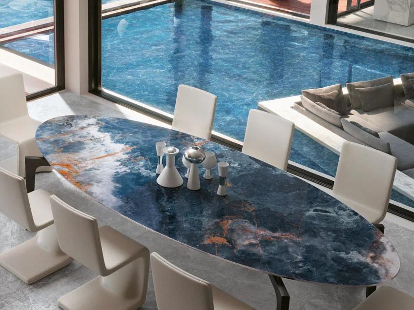 Oval dining table made with Ocean Blue porcelain slabs in modern poolside interior.