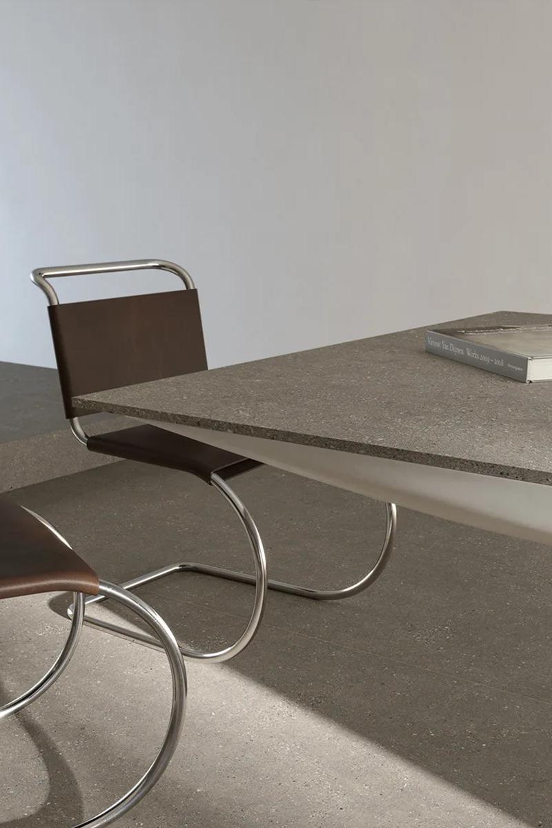Sandstone Warm porcelain slabs on a dining table paired with sleek chrome seating.