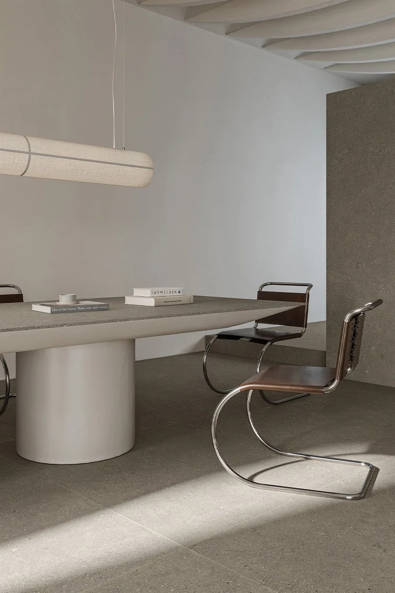 Sandstone Warm porcelain slabs on a pedestal dining table in a bright minimalist room.