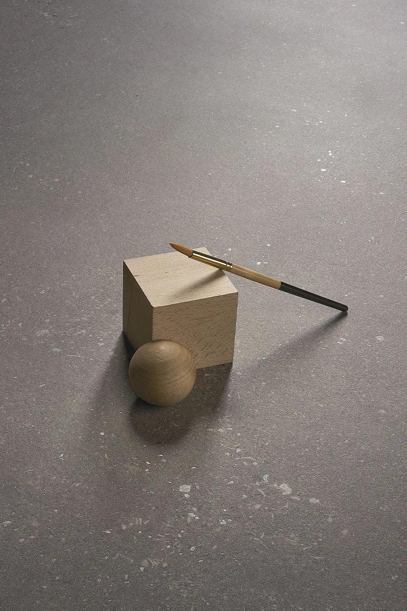 Surface detail of Sandstone Warm porcelain slabs with small wooden objects and mineral texture.