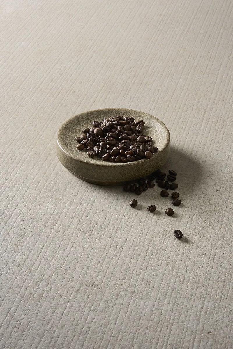 Bowl of coffee beans resting on the smooth matte surface of Fossil Row porcelain slabs.