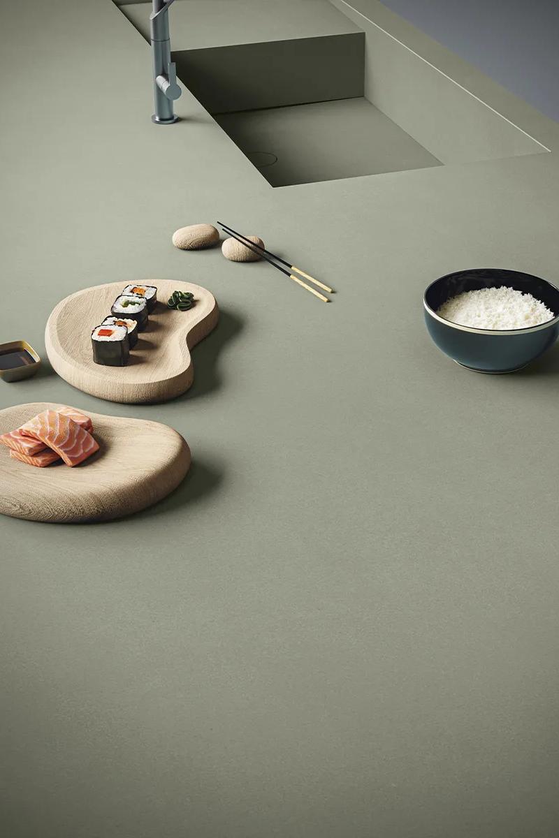 Gordes porcelain slabs in sage green with sushi dishes and wooden platters on top.