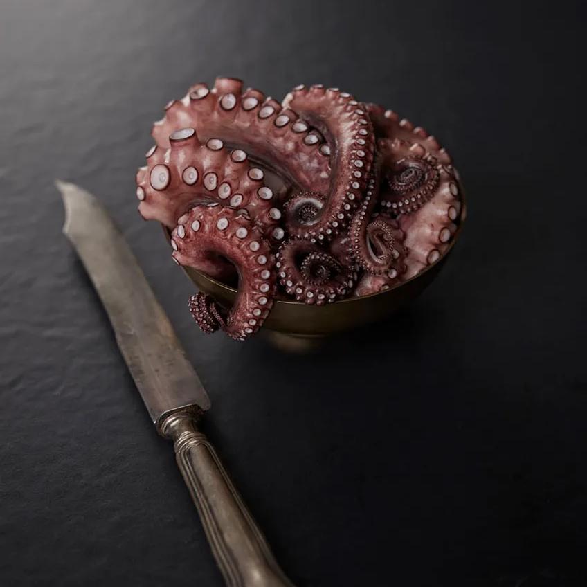 Whole octopus and vintage knife placed on deep black Pigalle porcelain slabs surface.