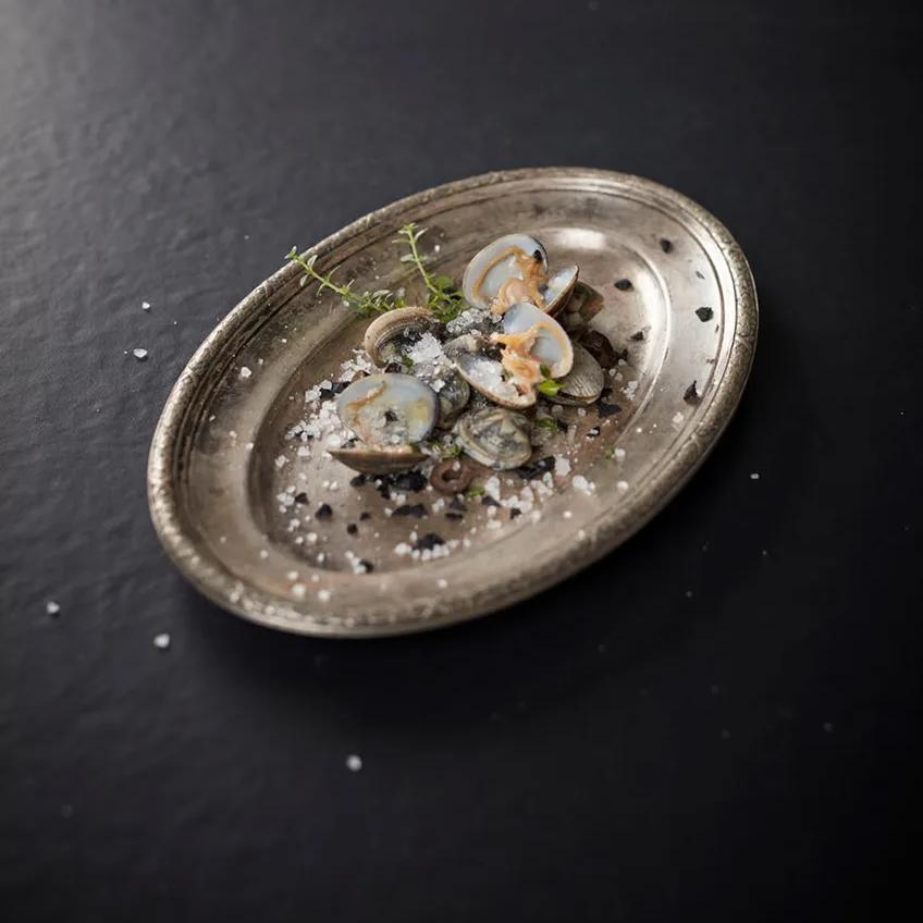 Silver platter with clams and shellfish displayed on Pigalle porcelain slabs background.