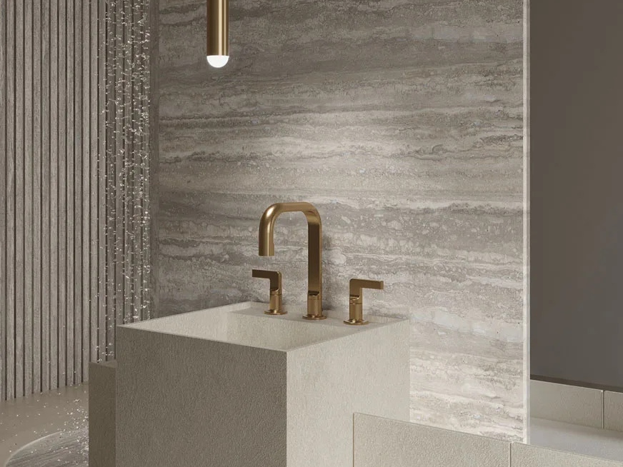 Travertino Trilogy porcelain slabs behind modern kitchen sink area with gold fixtures and pendant light.