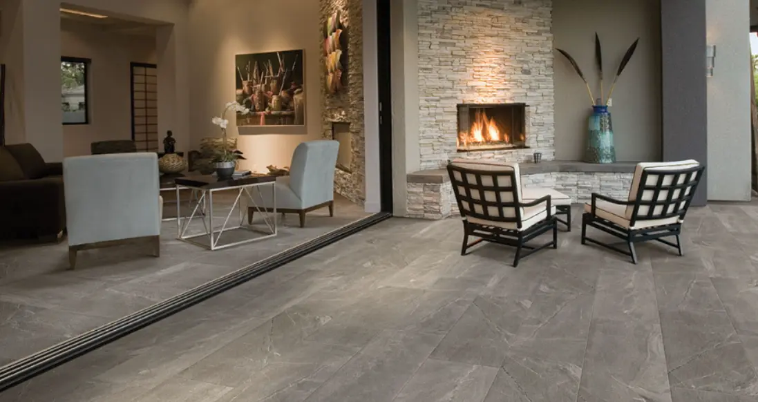 Modern indoor-outdoor living area with a fireplace and large slate look subway tiles on the patio flooring.