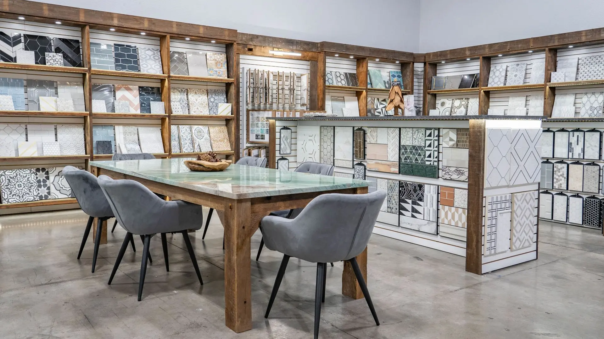 Nova Tile and Stone showroom displaying tile samples on wood shelves, with a central table and chairs.
