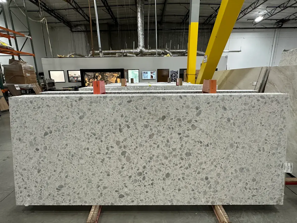 White engineered quartz slab with grey aggregate patterning displayed in a stone slab warehouse